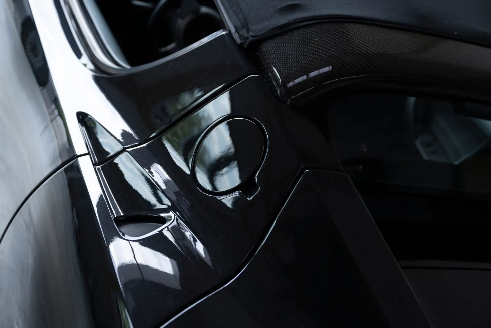 Detail on the flank of a black Tesla Roadster: the round charge-port flap and the transition to the scuttle, the hall reflected in the paint.